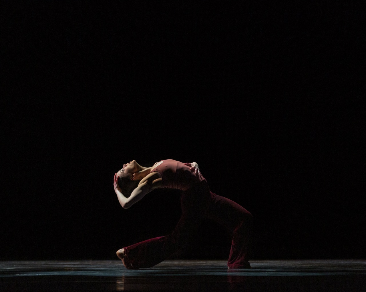 very dimly lit dancer doing a deep back bend with her hand above her head