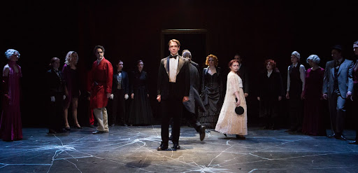 a performer in a suit stands centre stages as others look on from behind