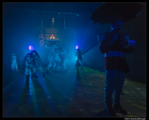 A dark theatre spaces with blue light and performers scattered about