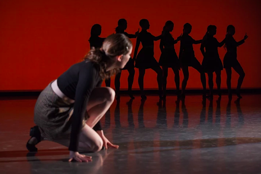 a performer crouches at the front of the stage while a row of others stand at the back