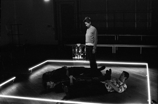 An actor stands in a square of light while others lie around them