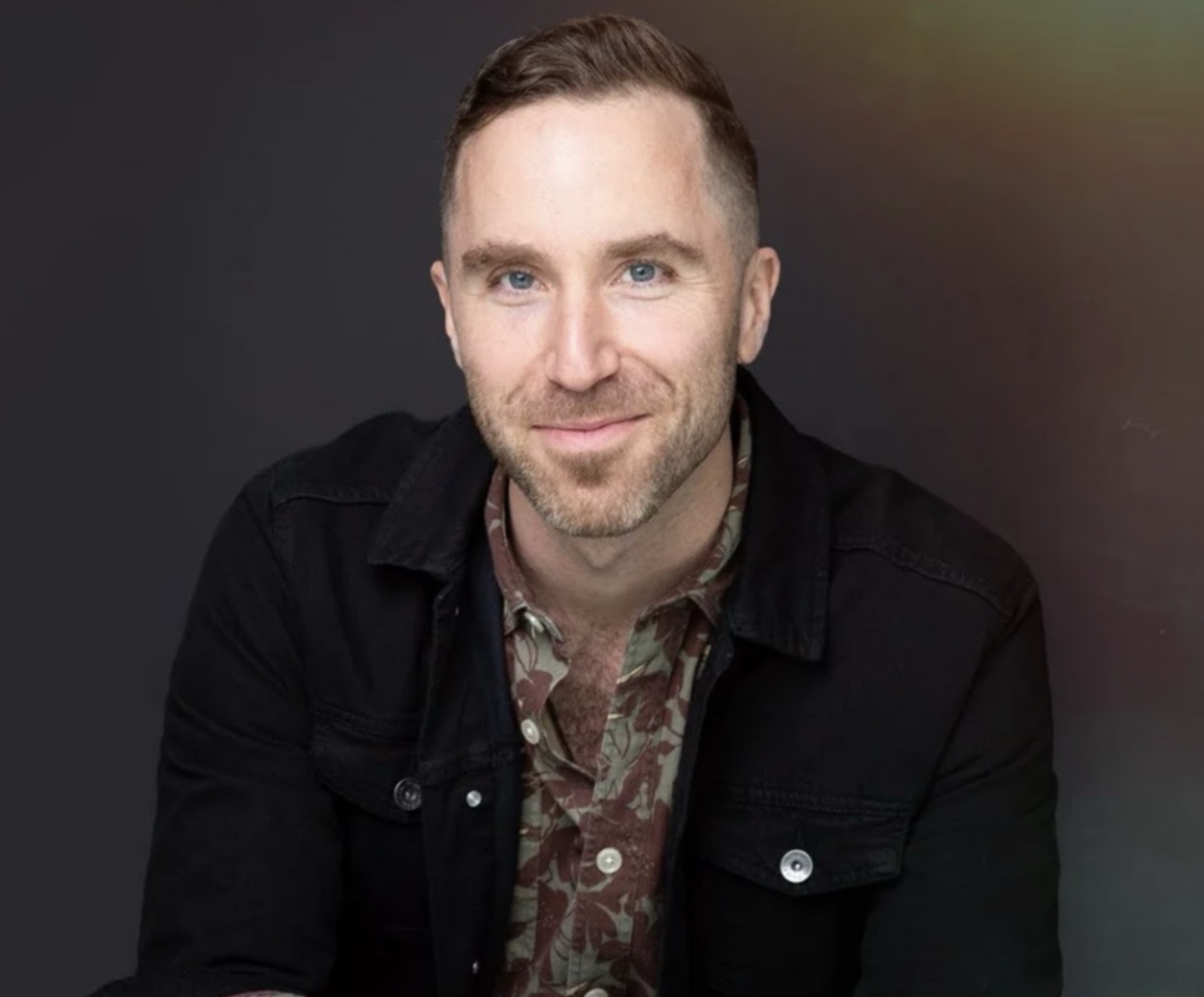 Peter smiles at the camera while wearing a floral button up shirt and black collared jacket.