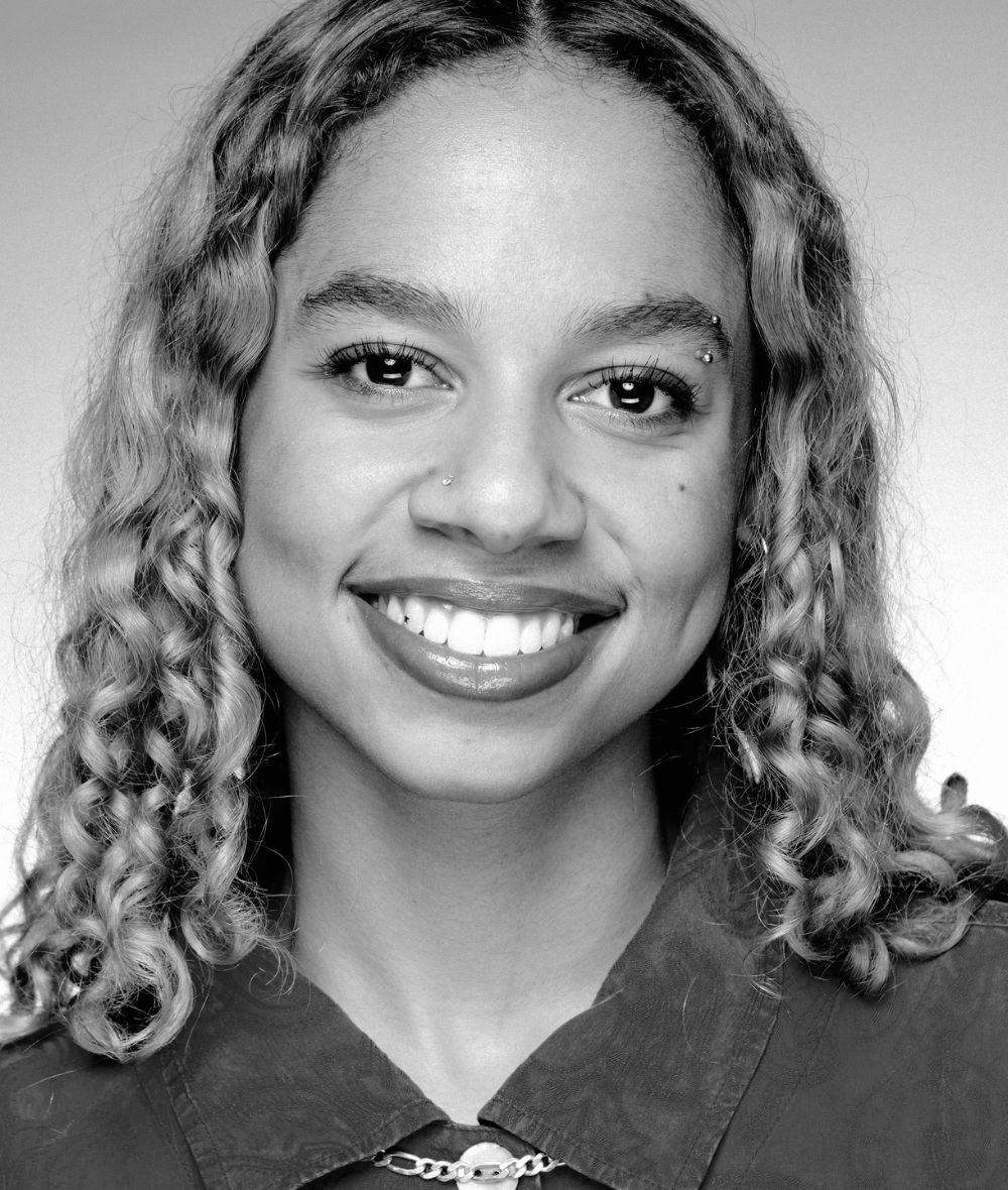 Millina's headshot is in black and white. Her hair is down and curly, and she smiles directly at the camera