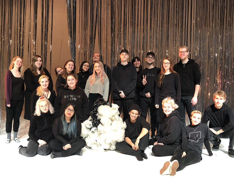 Alex and the production team stand as a group onstage 