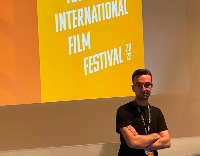 Alex stands in front of a Toronto International Film Festival Poster 