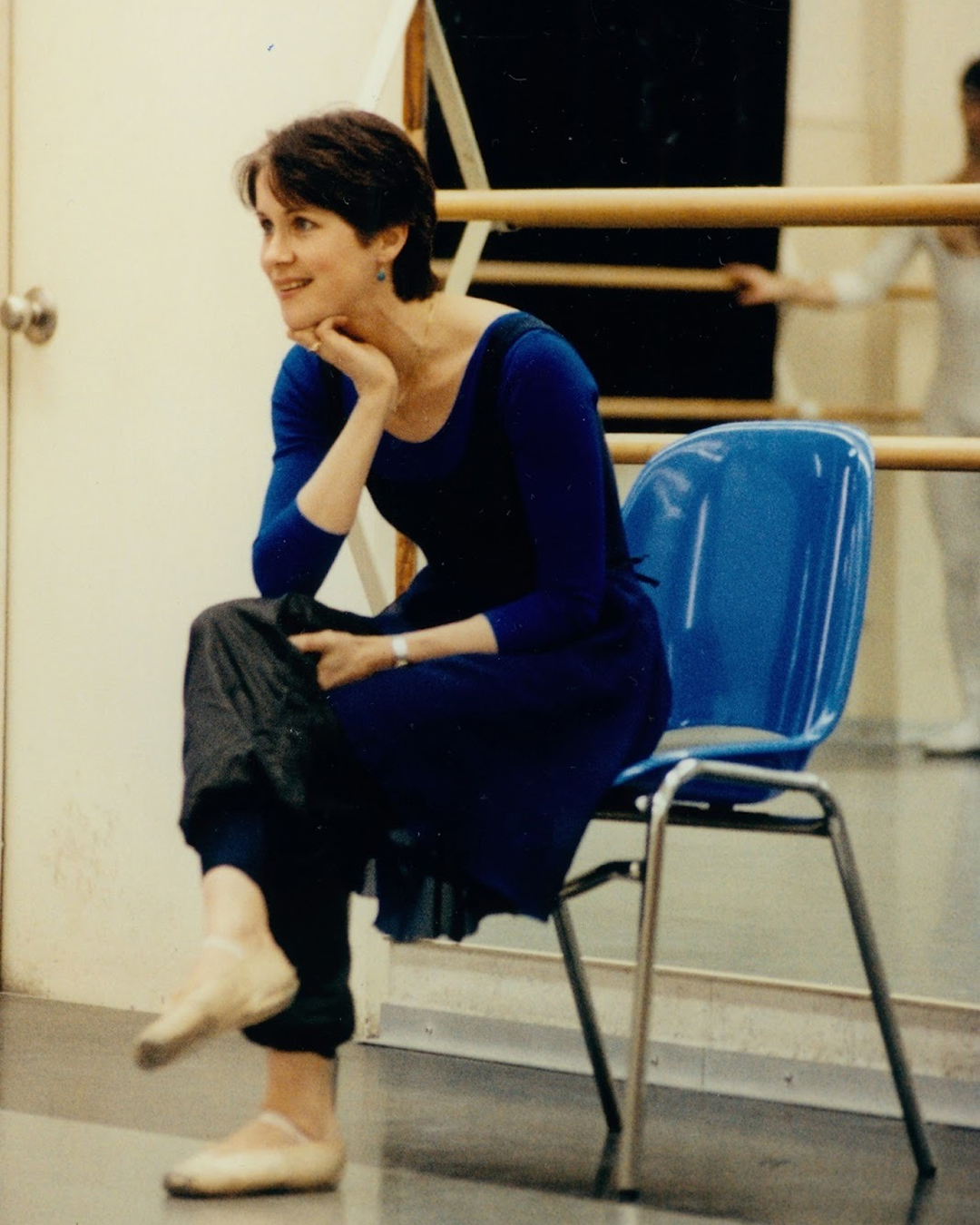 Nadia sits in a dance studio smiling while she watches a class off camera