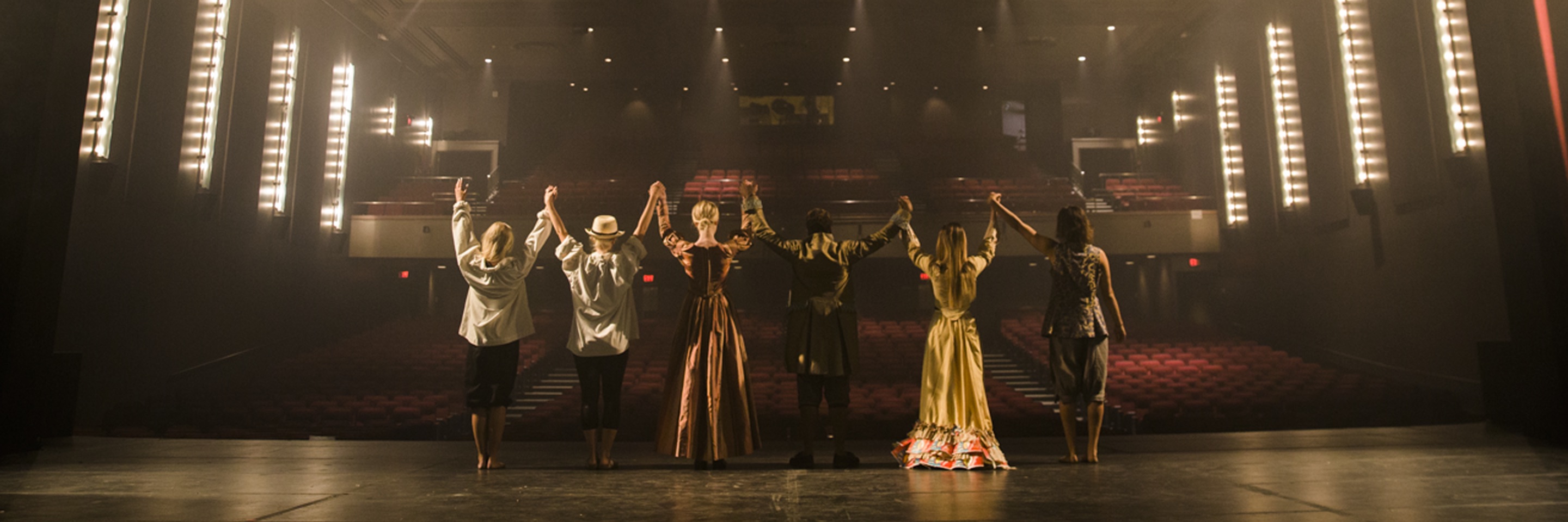 students stand onstage joyously holding hands in dance