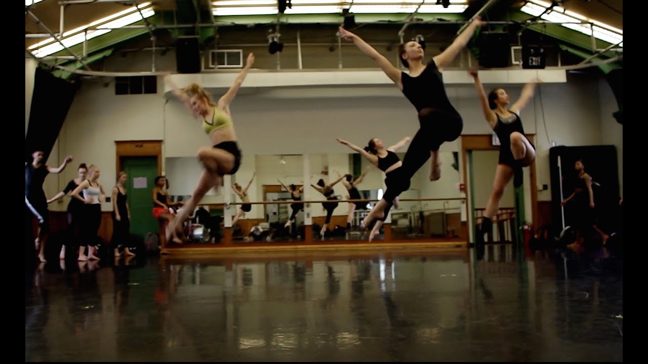 dancers jump in a studio with a barn-shaped roof