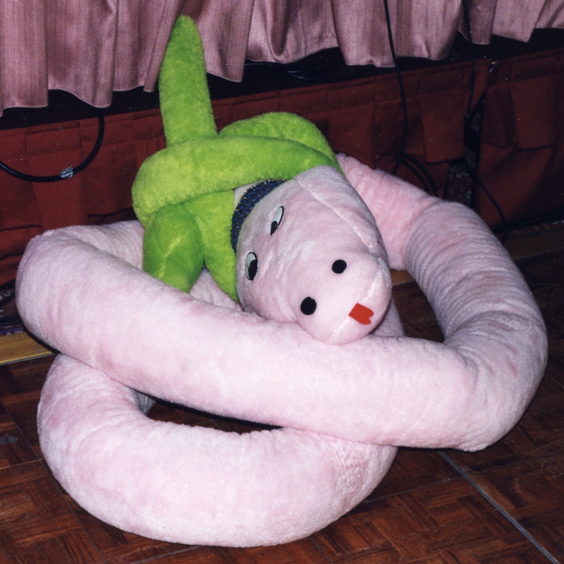 A stuffed pinked snakes with a green bow on its head.
