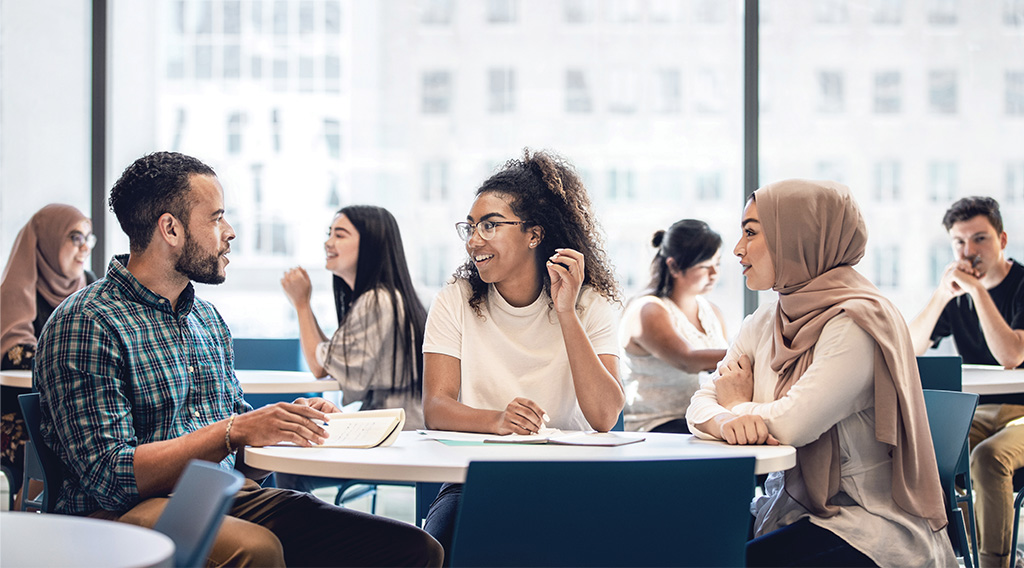 Students collaborating at a table with other students working at tables in the background