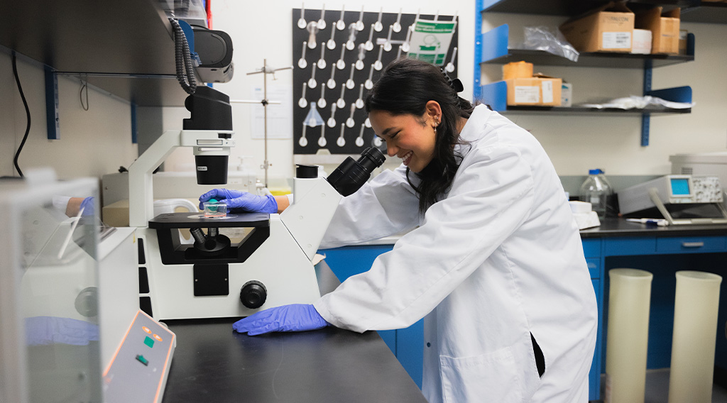 Student smiling while looking into a microscope
