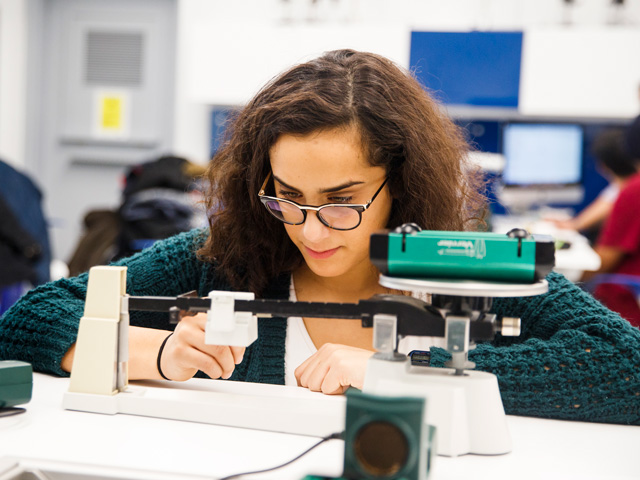 Physics undergraduate student calculating weight measurments in lab.