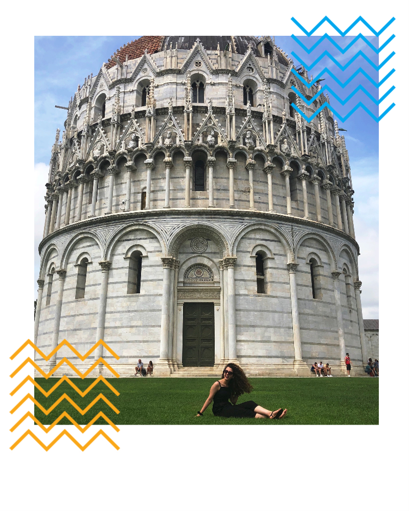 Zeina sitting on the grass in front of a circular architecture in a city in Europe