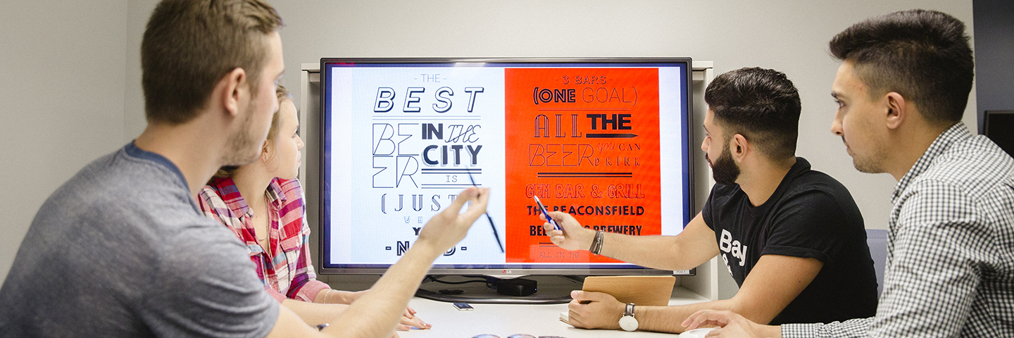 Four students working together at a table, analyzing a design on a screen.