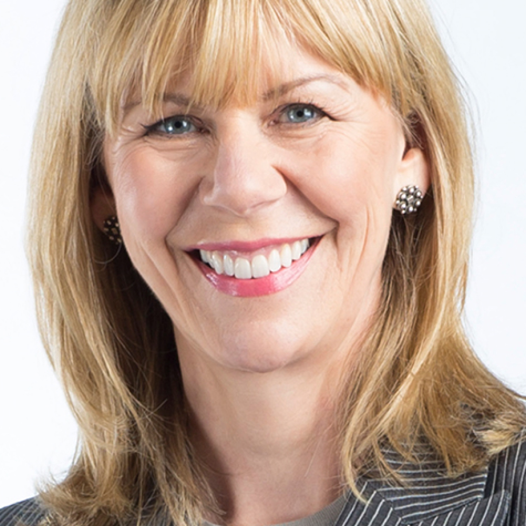 Close-up headshot of Alison Smith smiling. She has blonde hair with bangs and is wearing a grey pinstripe blazer with stud earrings.