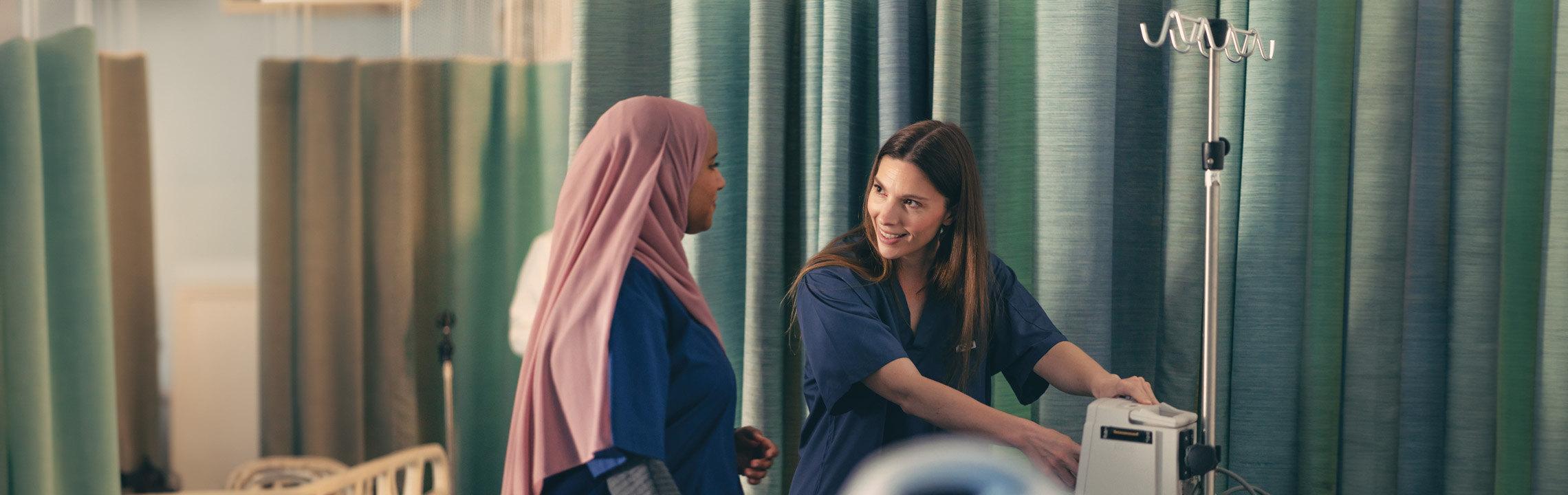 A pair of Nursing students chat while setting up an IV pole.