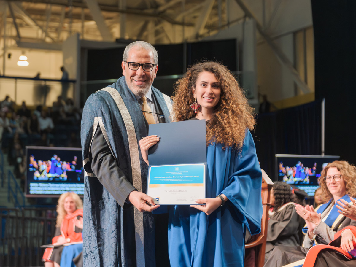 Samin Barakati, in a blue graduation robe, is presented with the TMU Gold Medal Award by TMU president, Dr. Mohamed Lachemi.