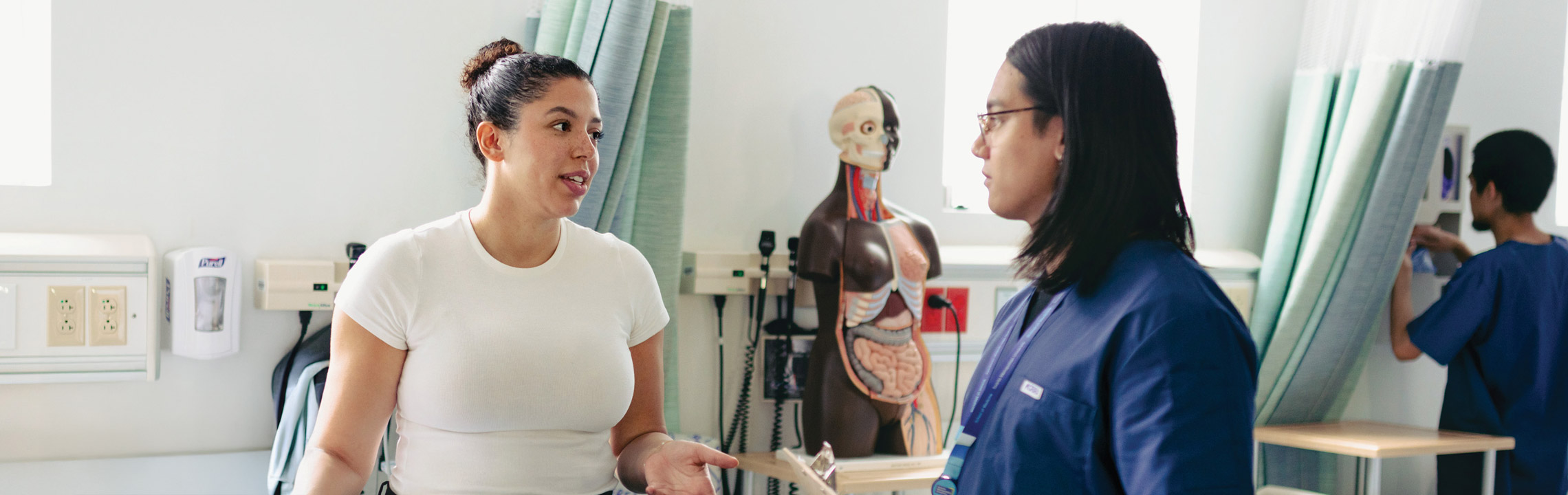A nurse listens attentively to a patient in a sunny hospital room.