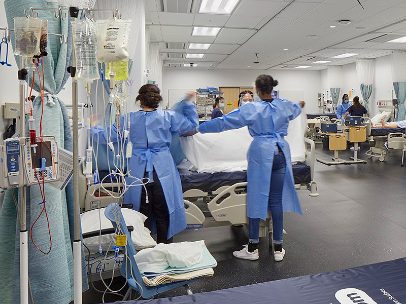 Nurses wearing a medical gown around a patient in bed in a medical facility.