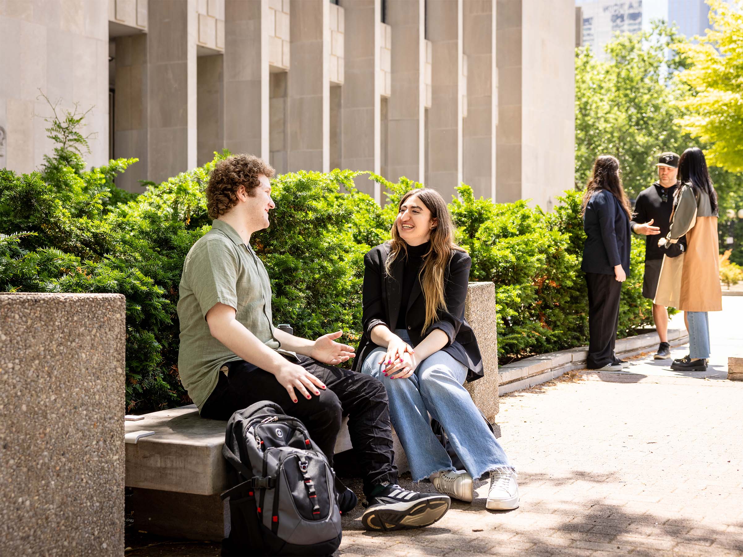 A pair of students talk animatedly outside the Toronto Courthouse on a sunny day.