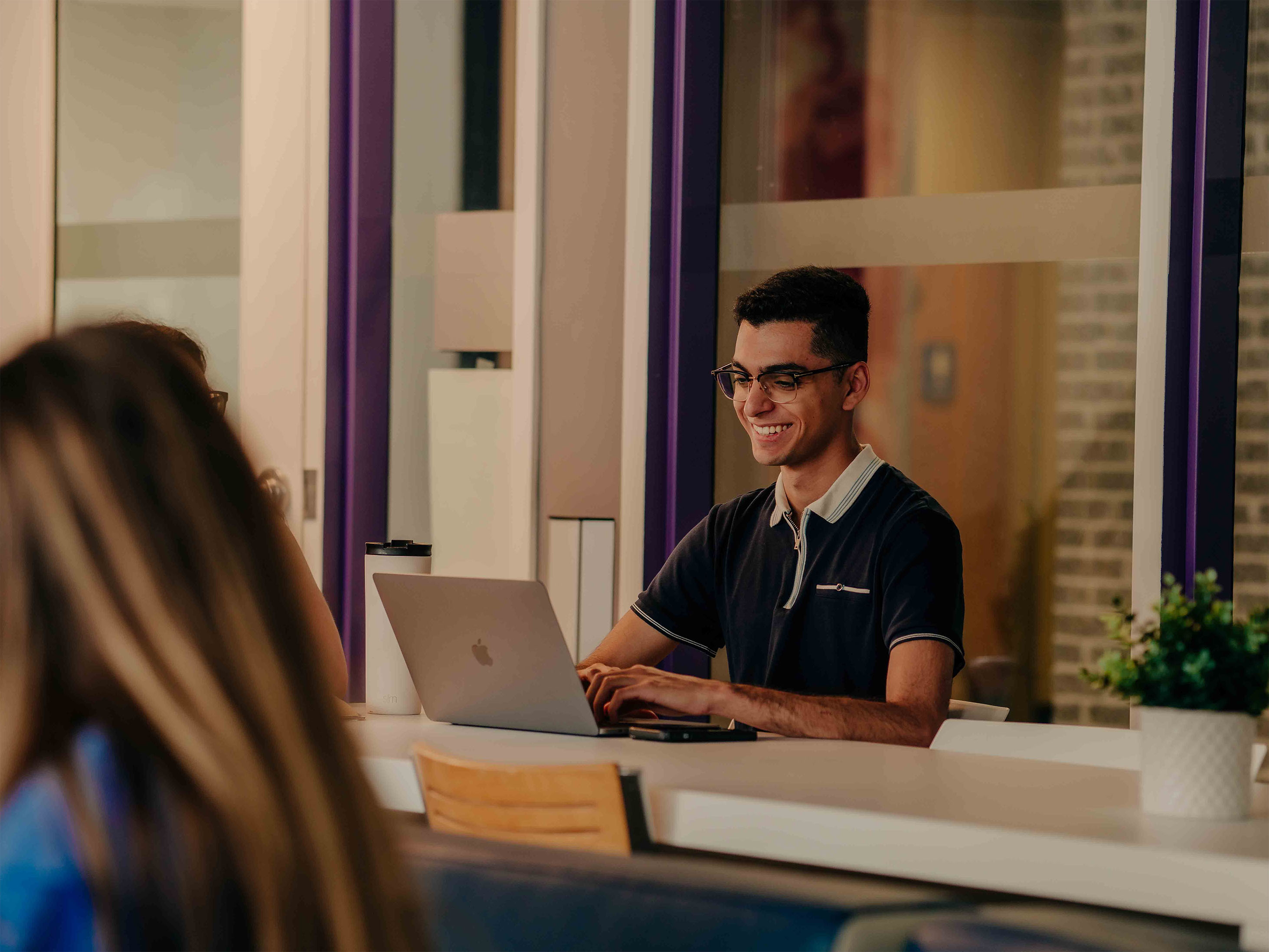 A student smiles at their computer screen while working on campus.