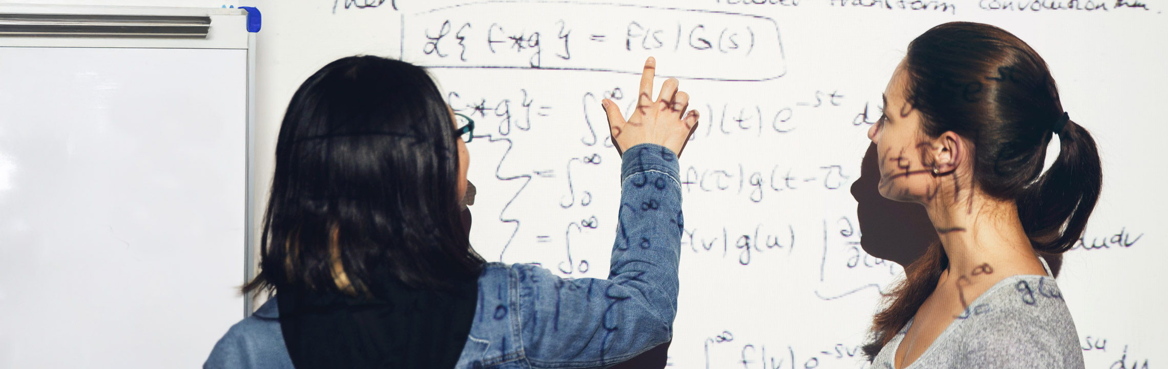 A pair of students review an equation on a board in a classroom.