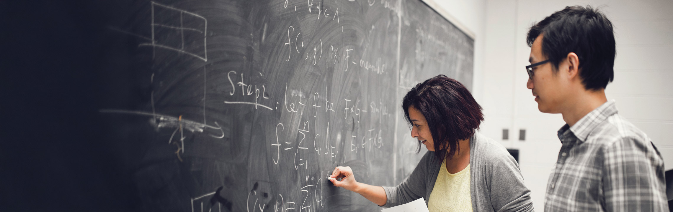 A pair of students work on an equation together on a blackboard.