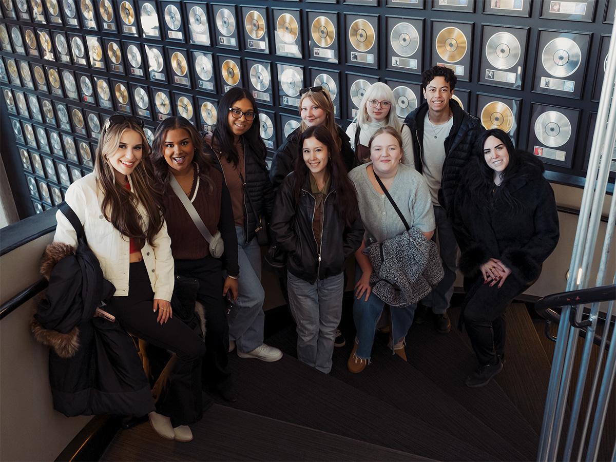 A group of Professional Music students gather for a group photo by a wall of music awards in Nashville.