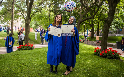 Two female students at convocation holding their degrees