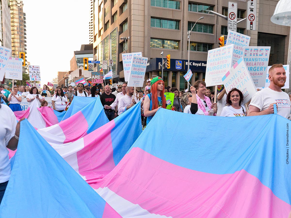 Pride Parade marchers walk holding large Transgender Pride flag - Credit to Photovyu via Dreamstime.com