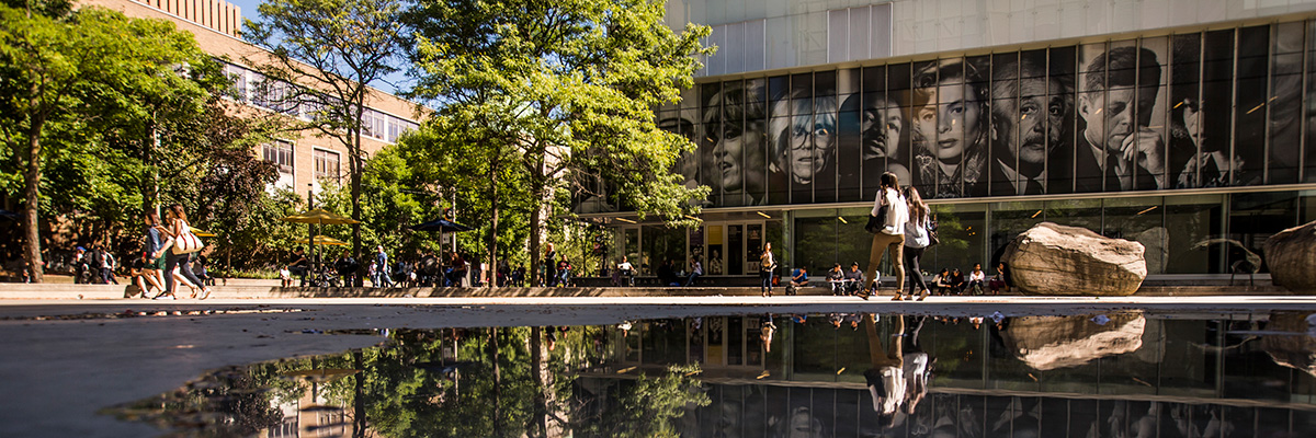 People walking around Lake Devo with reflections of the trees and buildings in the water.