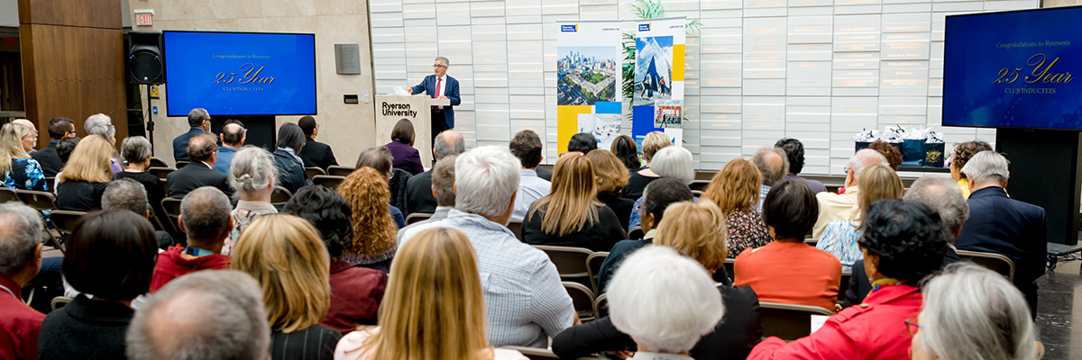 A large audience of people sitting listening to a speaker at the podium at the front of the room.