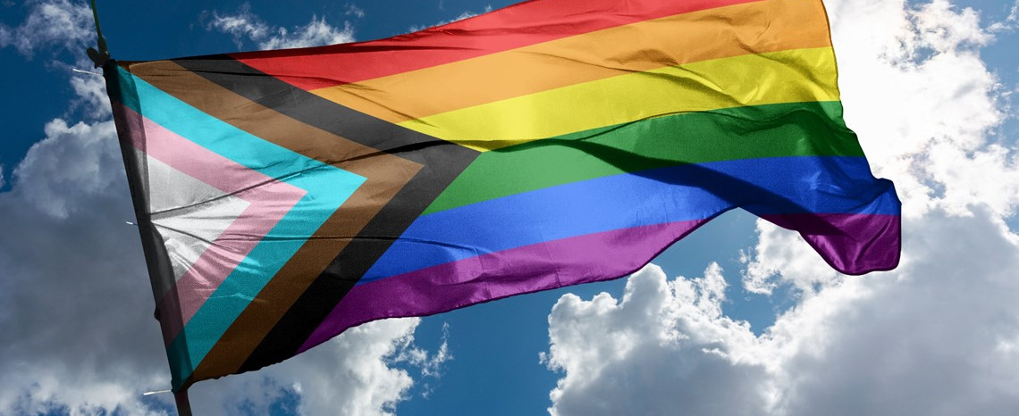 Pride Progress Flag flying against a blue sky