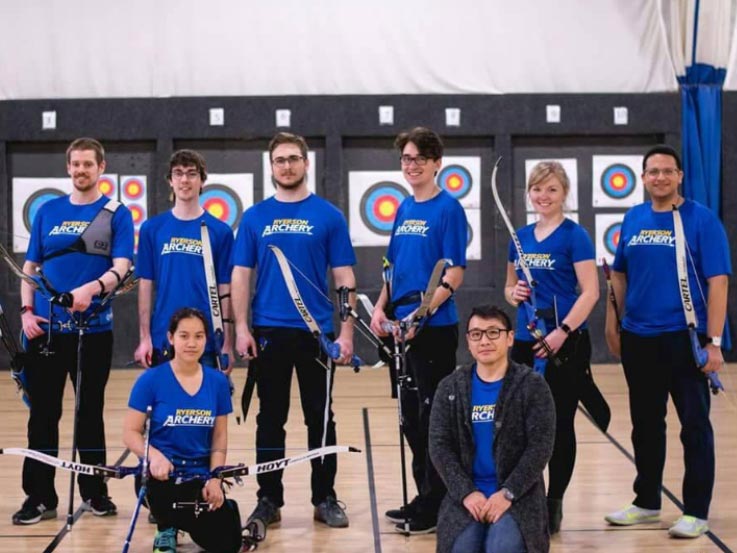 Ryerson Archery Club poses with their equipment and targets behind them.
