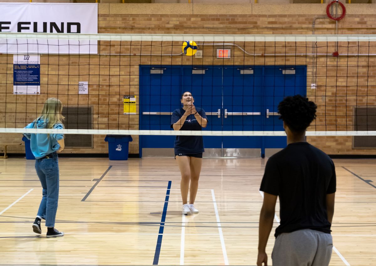 Three females players at the net with a volleyball.