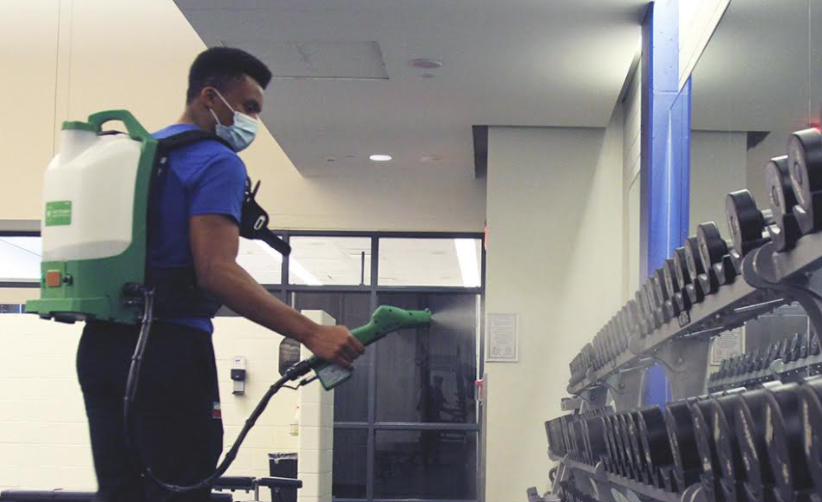 Athletics & Recreation staff member using an electrostatic sprayer to clean free weights at the Mattamy Athletic Centre