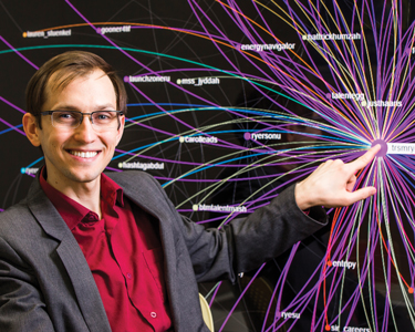 Business Management Researcher, Anatoliy Gruzd, stands in front of an intricate relational graph. 