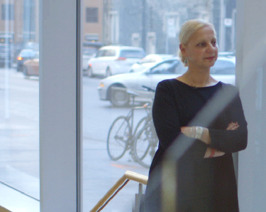Mechanical and Industrial Engineering Researcher, Ayse Bener, stands with arms crossed in front a large window.