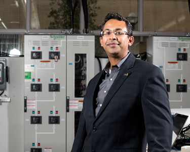 Electrical and Computer Engineering Researcher, Bala Venkatesh, stands in front of large computer terminals. 
