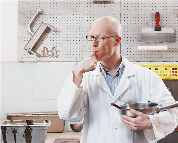 Chemistry and Biology Researcher, Dérick Rousseau, wears a white smock and licks batter from his finger. 