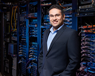 Electrical and Computer Engineering Researcher, Ebrahim Bagheri, stands in front of large computer terminals with exposed wires.