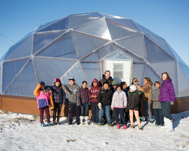 Students stand in front of a geodesic growing dome. 