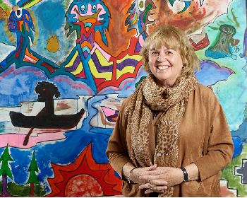 Child and Youth Care Researcher, Judy Finlay, stands in front of a colourful, hand-painted mural. 