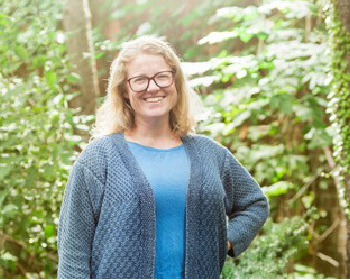 Chemistry and Biology Researcher, Lesley Campbell, stands in a forested area. 