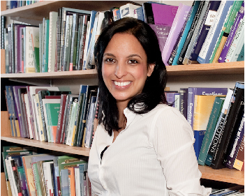 Psychology Researcher, Naomi Koerner, stands, smiling in front of a large bookshelf.