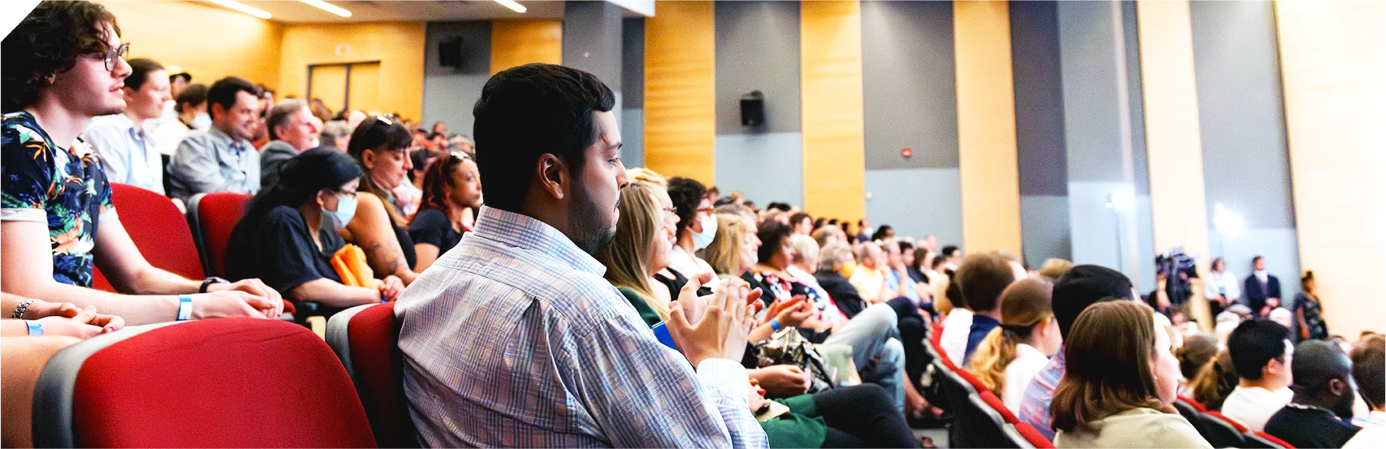 A group of people sitting in an auditorium stare forward, attentively.