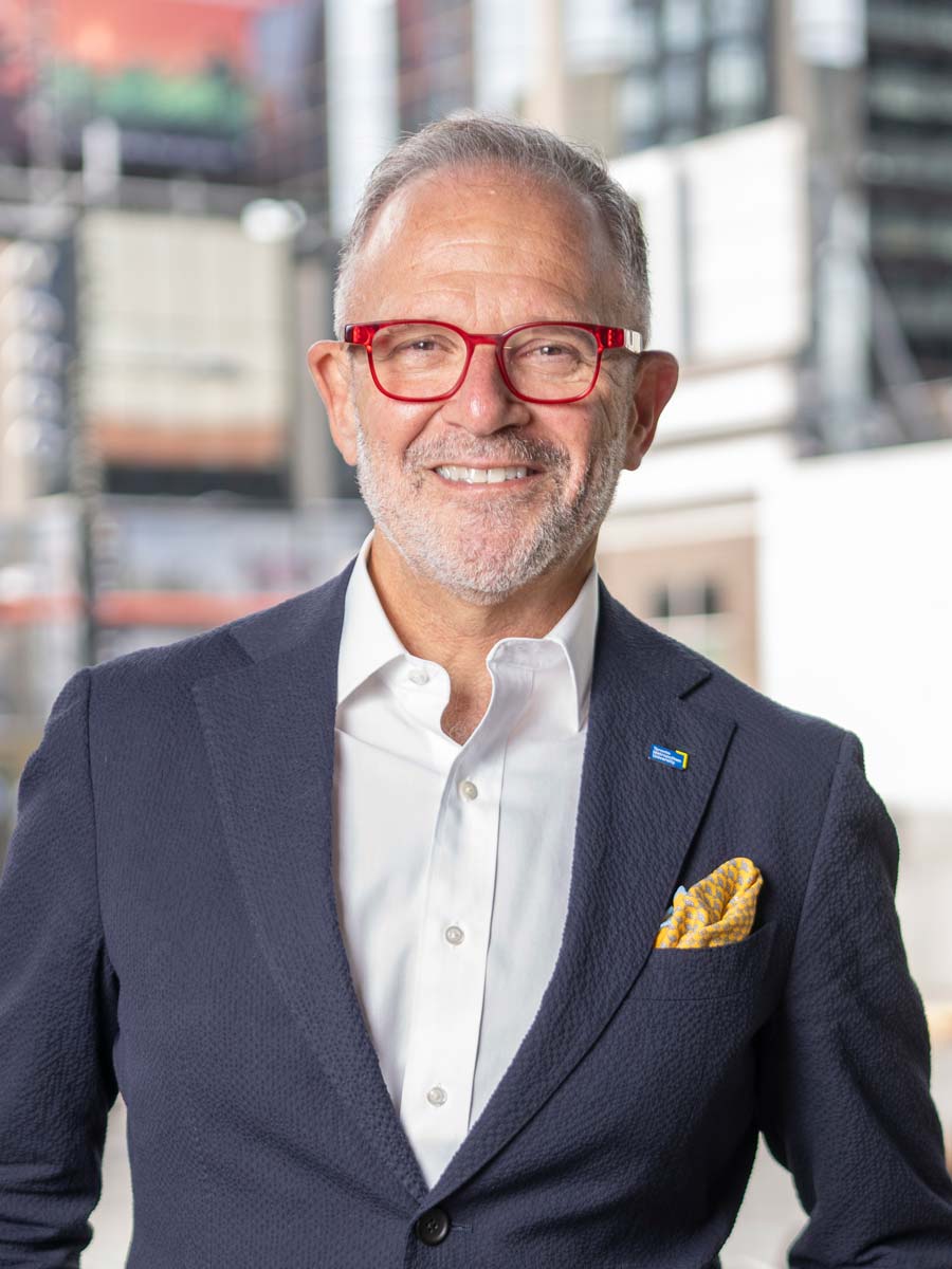 Toronto Metropolitan University's Vice-President, Research and Innovation, Steven N. Liss, stands smiling with the university's urban campus out-of-focus behind him.