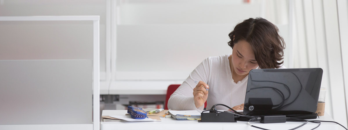 A single female student intently studying at a desk in front of a laptop 