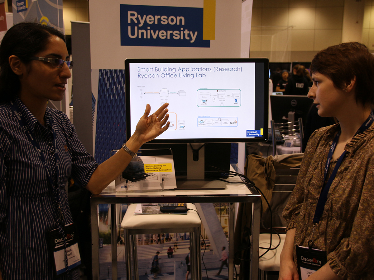 Two women talk in front of a screen that reads "Smart Building Applications (Research) Ryerson Office Living Lab"