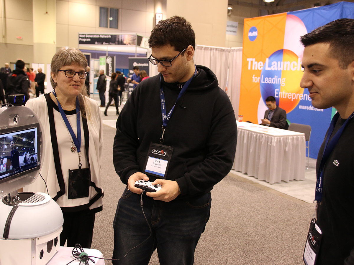 An attendee of OCE Discovery handles a game controller and stares intently at a screen while observed by two researchers